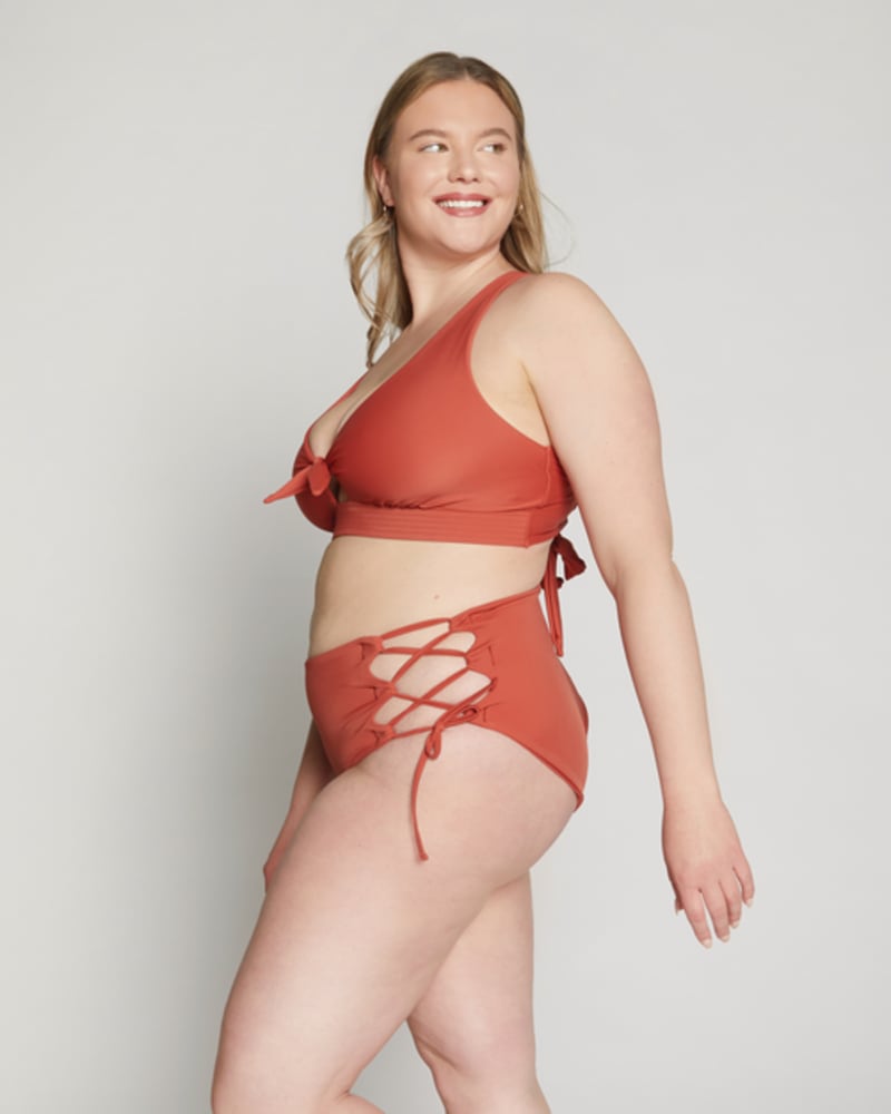 Side of a model wearing a size 10/12 Lola Side-Tie Bottoms in Terracotta by Wild Isles. | dia_product_style_image_id:251710